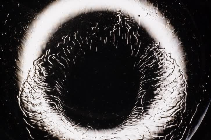 Abstract macro time-lapse of a liquid freezing into intricate, feathery ice crystals around a circular light source