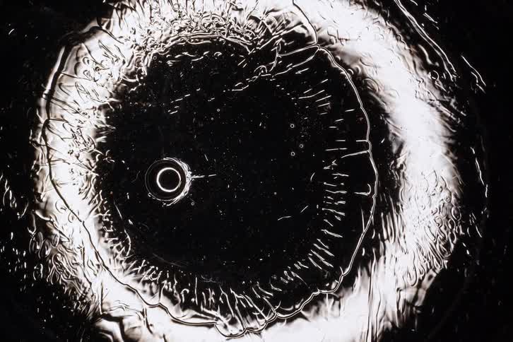 Hypnotic macro view of clear liquid bubbles slowly merging and changing shape against a dark background