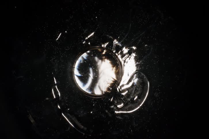 Hypnotic overhead view of an abstract chemical reaction as white ink diffuses through a clear liquid in a circular pool