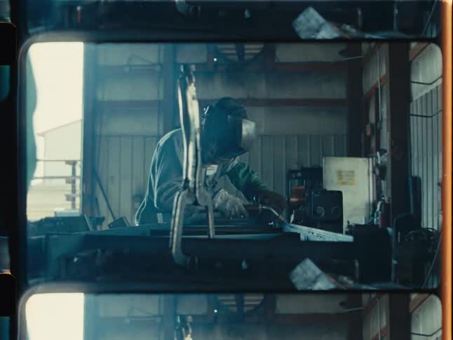 Vintage film style shot of a welder meticulously working on a steel beam in a hazy industrial factory