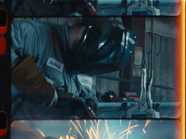 A welder in a protective helmet creates sparks while working on metal in a workshop, captured on vintage film