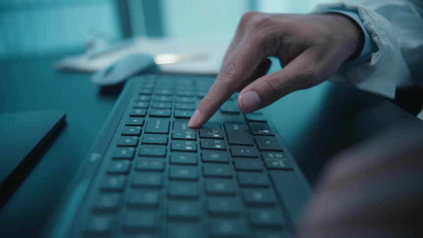 A close-up slow-motion shot shows a professional's hands typing on a keyboard and pressing the enter key in a modern office