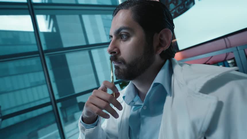 A pensive neurologist examines a series of brain scans on his computer before pausing to reflect on the diagnosis