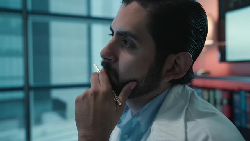 A focused doctor in a lab coat thoughtfully analyzes medical data on a large screen in his modern office