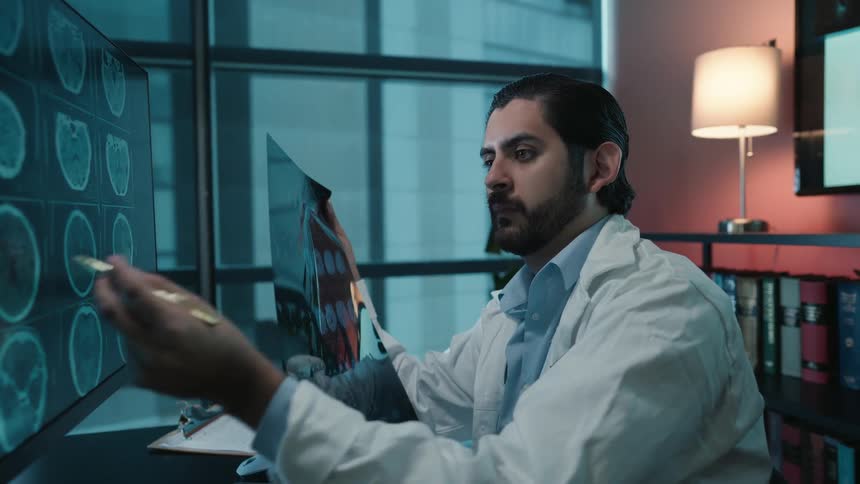 A focused doctor in his modern office compares a patient's brain scans on a computer monitor with a physical X-ray