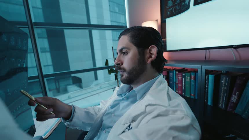 A focused doctor in a lab coat carefully examines an MRI scan in his modern office, using a pen to analyze the details