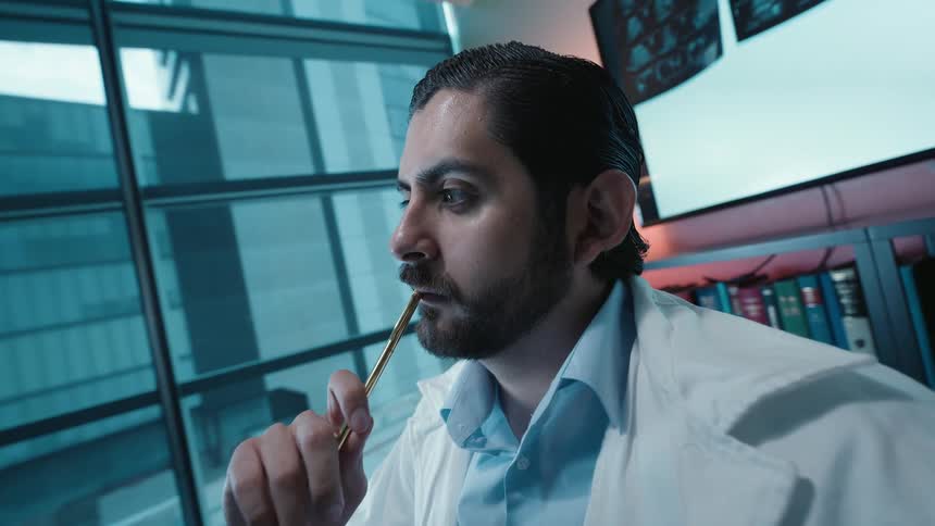 A pensive doctor in a lab coat analyzes a patient's CT scans on a large monitor in his modern office