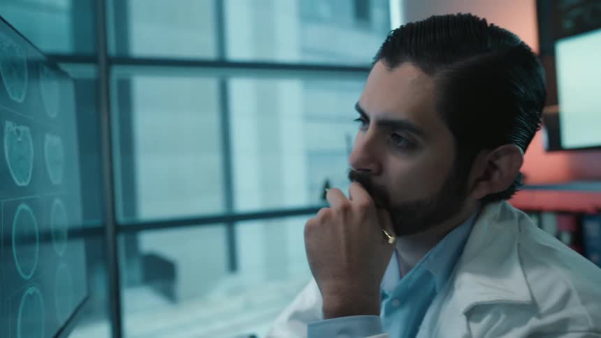 A thoughtful neurologist carefully examines a patient's brain scan on a computer monitor, pointing out key areas for diagnosis in his modern office