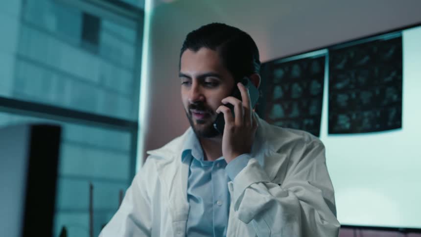 A doctor analyzes human brain scans on a large digital screen before discussing the diagnosis on a phone call in his modern office