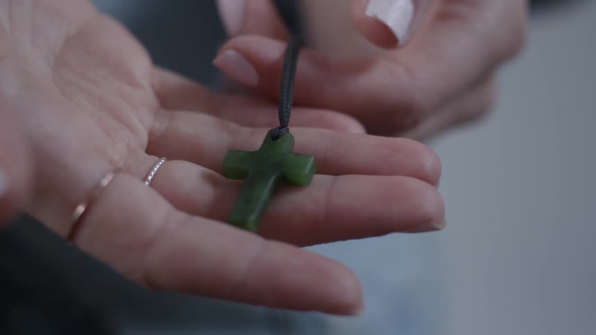 A woman holds a cross necklace in her hand