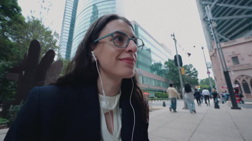 Happy businesswoman takes a break from her laptop, listening to music on her earphones while sitting on a city bench