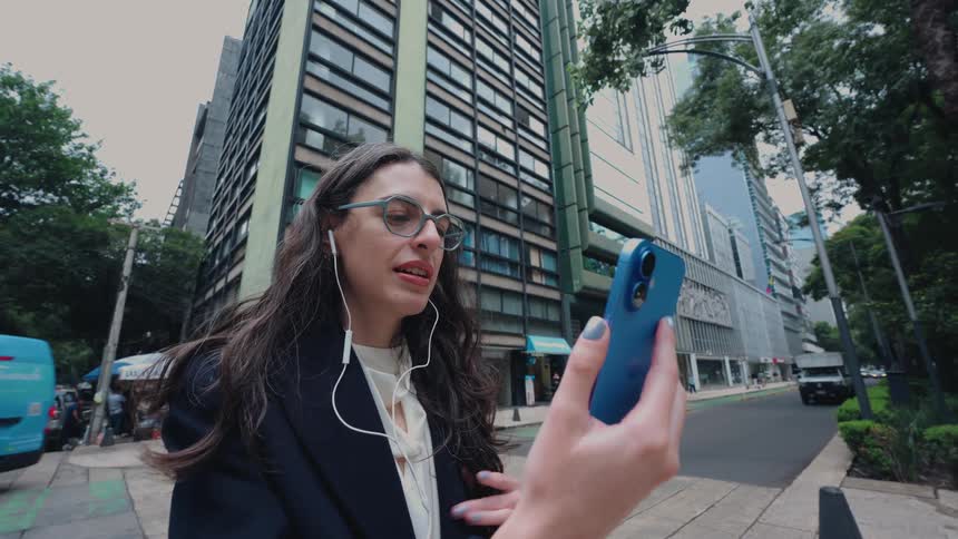 A professional woman has a video conference call on her smartphone while standing on a busy city street