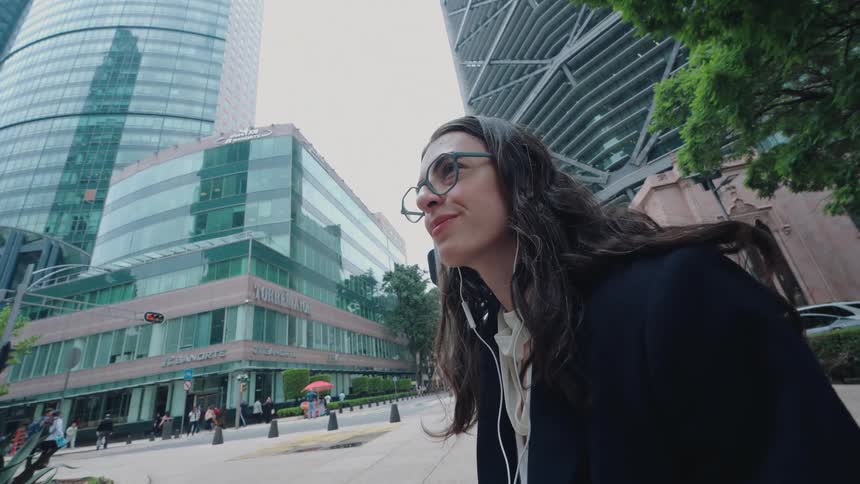 Stylish businesswoman enjoys a moment of peace, listening to audio on her phone while sitting on a bench in a bustling financial district