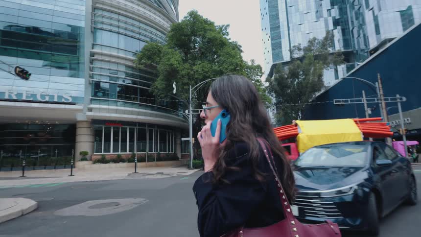 A businesswoman talks on her cell phone while walking on a busy street in a modern city in slow motion