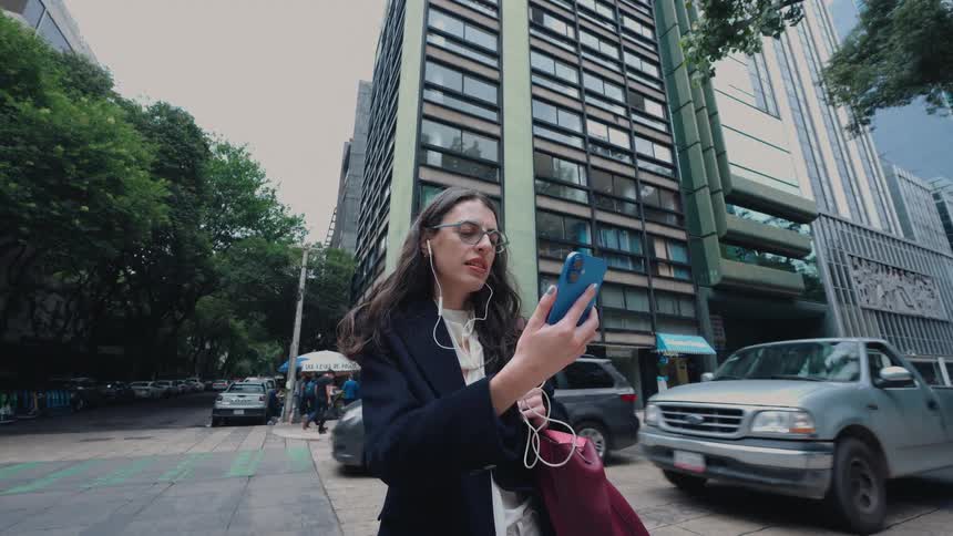 A young professional woman has a video call on her smartphone while standing on a busy downtown street corner