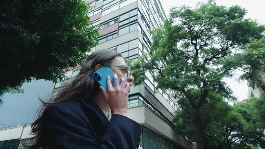 Low-angle shot of a stylish woman with glasses answering her smartphone on a city street next to a tall building
