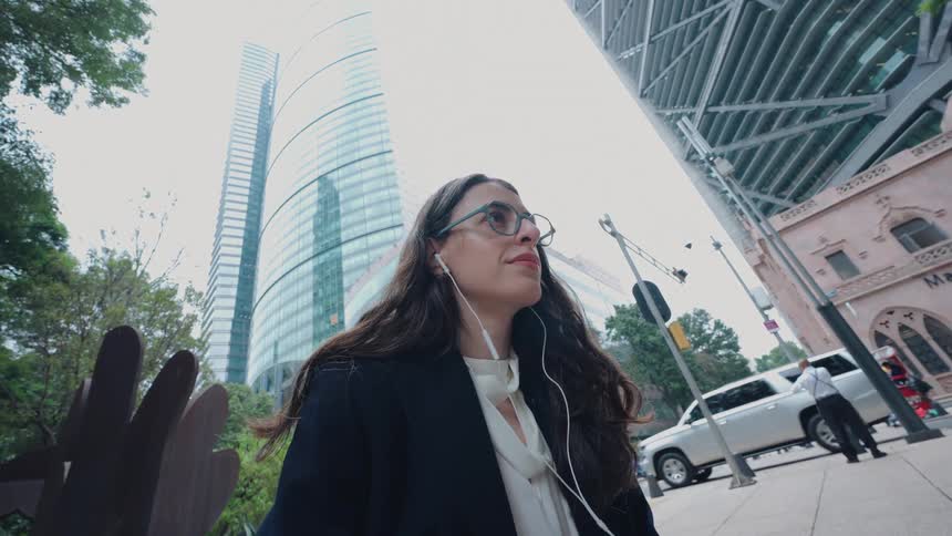 A young businesswoman closes her laptop and enjoys a moment of calm listening to music on a bustling city street surrounded by modern skyscrapers