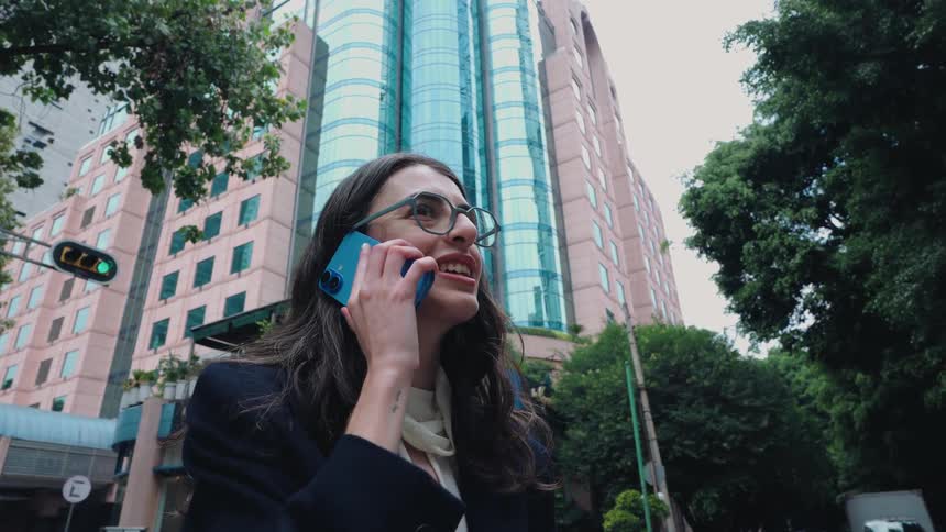 Low angle shot of a businesswoman in glasses talking on her phone in a city with a modern skyscraper in the background