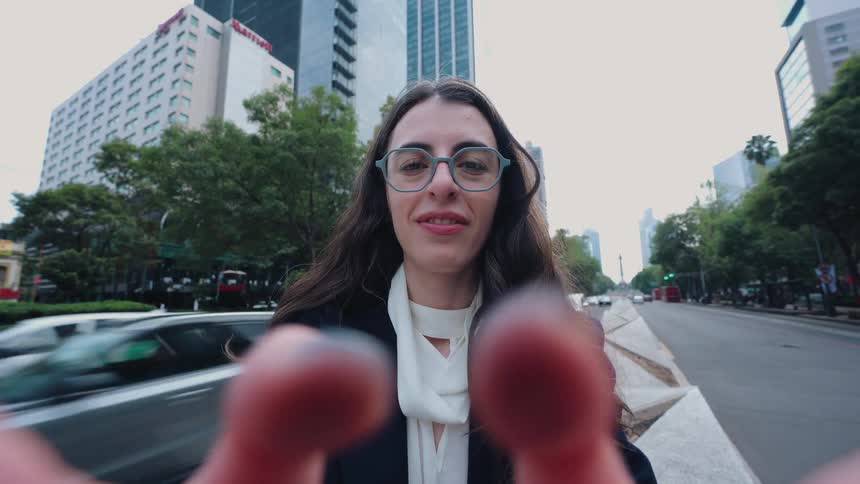 Cinemagraph of a stylish woman holding the camera for a selfie video on a busy city street with traffic moving in the background