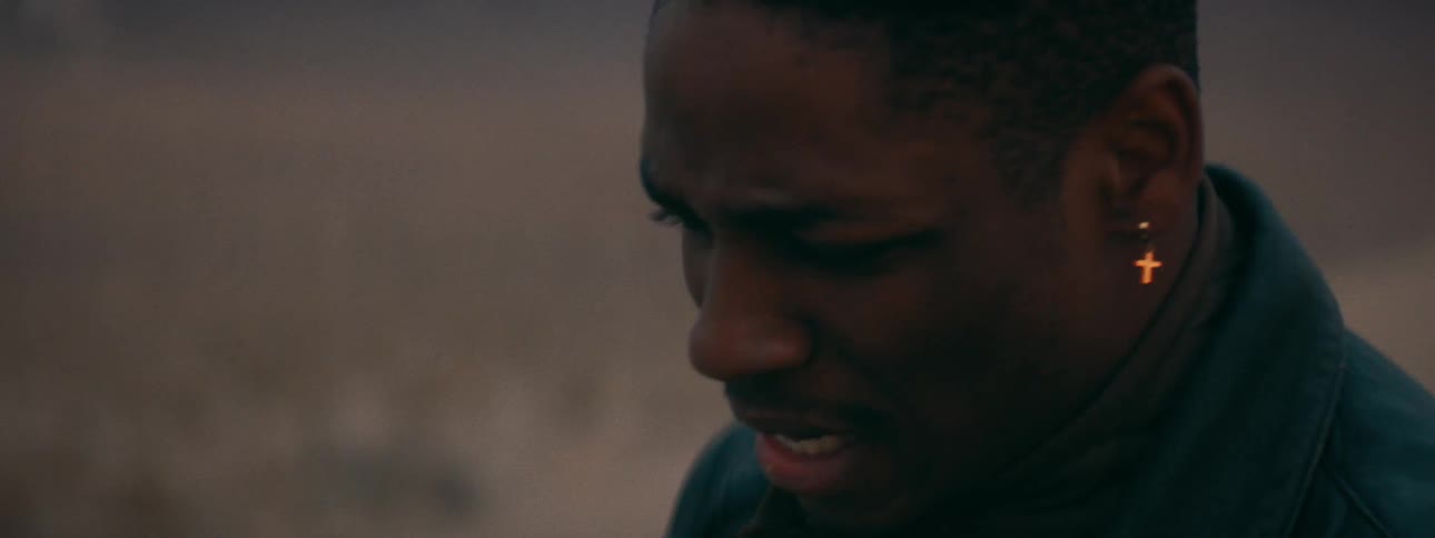 Dramatic close-up of a sorrowful young man with tears in his eyes, looking down in despair at dusk