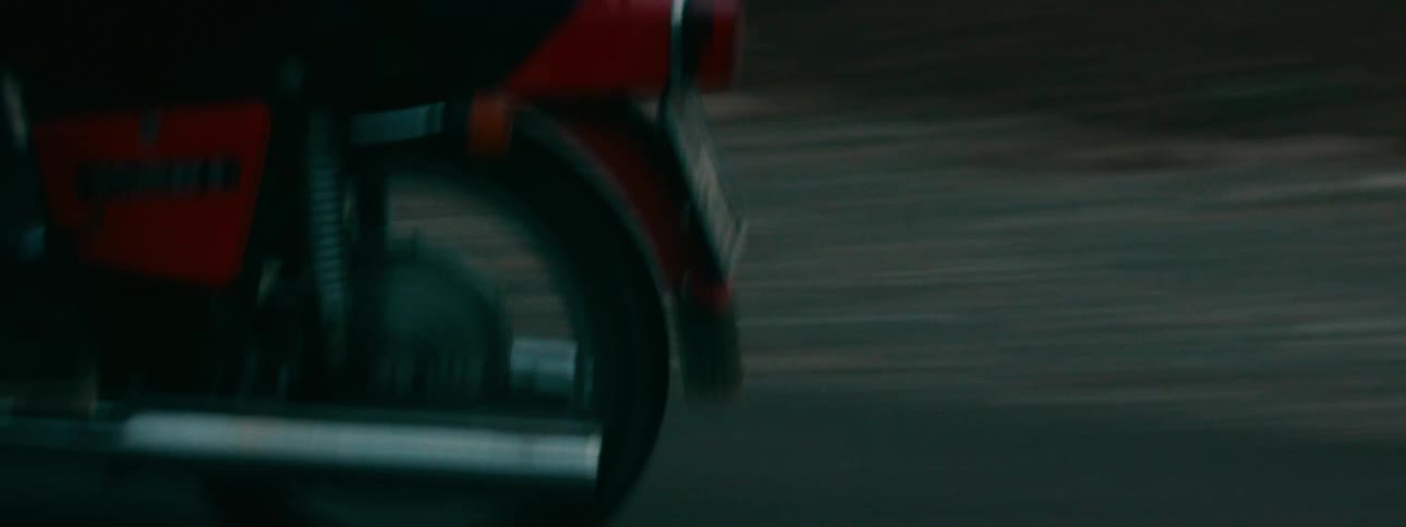 A close-up shot of the rear wheel of a vintage red motorcycle as it speeds down the road