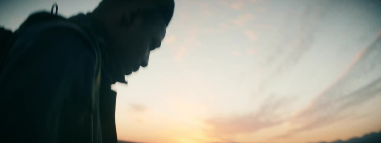 A lone traveler with a backpack looks down thoughtfully before walking into the vast desert landscape at sunset
