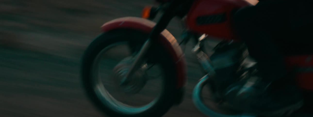 A close-up of a red vintage motorcycle's front wheel spinning as it cruises down a road during golden hour