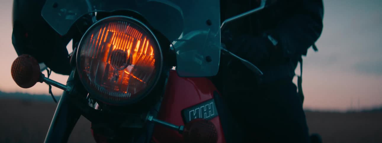 Close-up of a vintage motorcycle headlight turning off with a cinematic lens flare at dusk