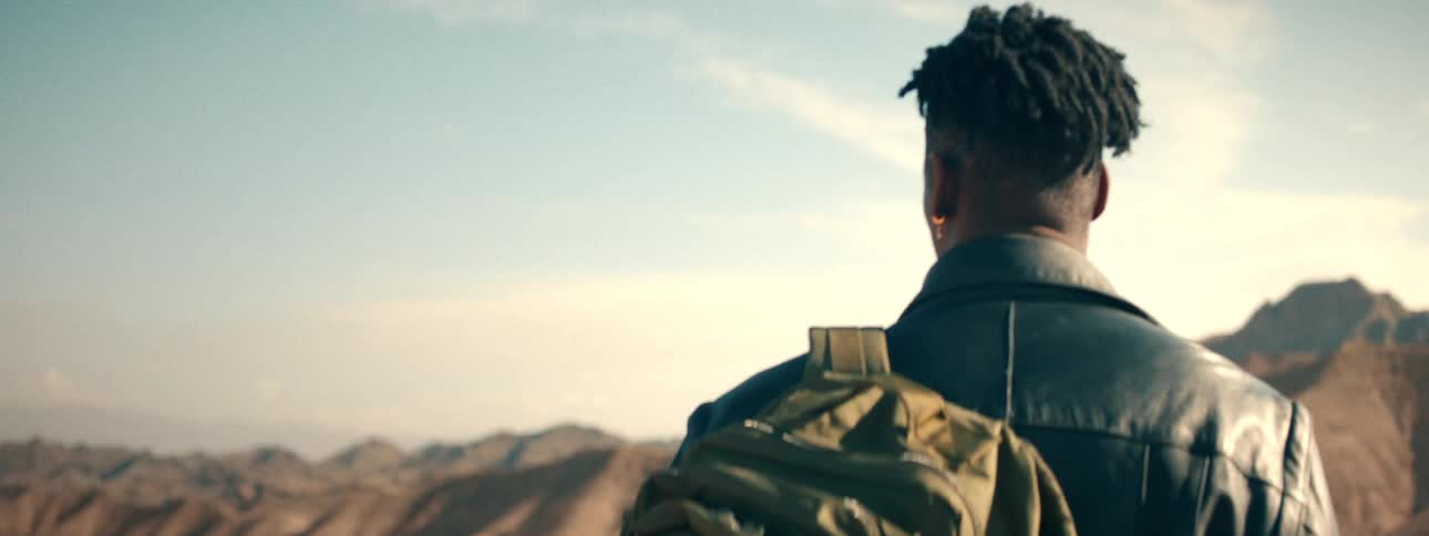 Cinematic slow focus shot of a traveler from behind as he looks out over a vast desert mountain range