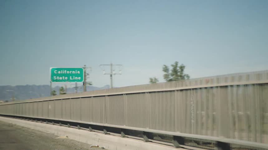 A slow motion shot from a car driving past the California State Line sign on a sunny day