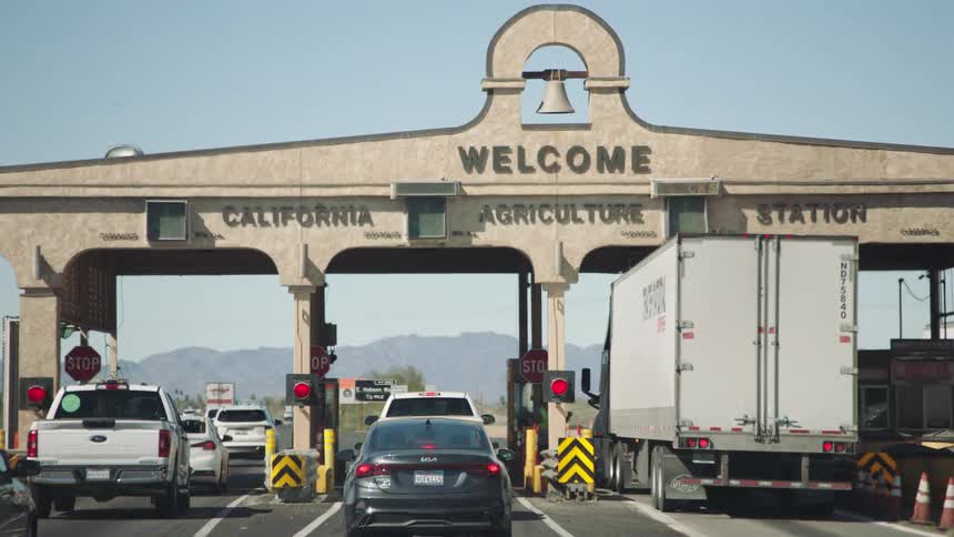 Vehicles slowly approach the California Agriculture Station border inspection point on a sunny day in the desert