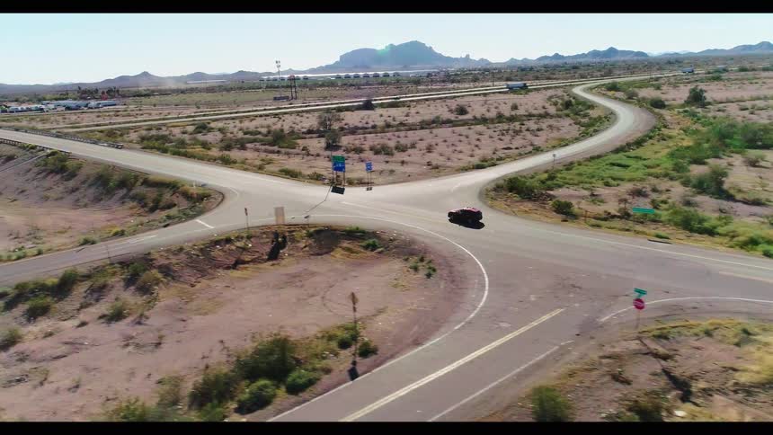 An aerial view captures cars and trucks driving along a highway interchange in a vast, arid desert landscape
