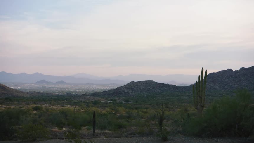 A slow pan reveals a vast desert valley with saguaro cacti and a cityscape nestled among the mountains at dusk