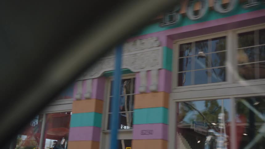 Driving past the iconic and colorfully painted "Circus of Books" storefront on a sunny street in Los Angeles