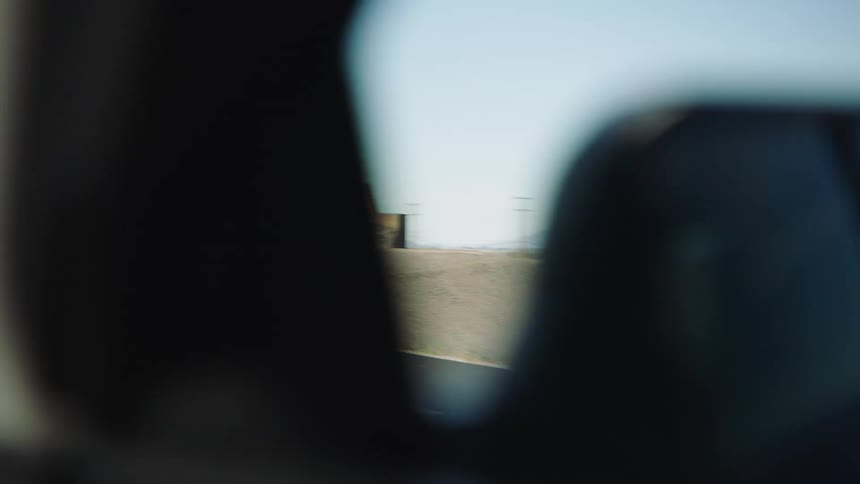A slow-motion passenger view driving past the iconic 'California' welcome sign on a desert highway