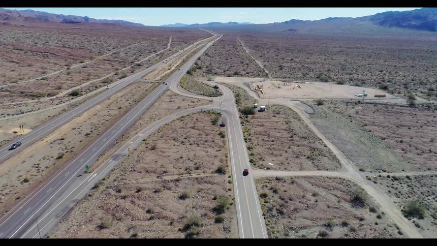 Ascending aerial shot of a red car driving on a lonely road through a vast desert landscape towards a highway