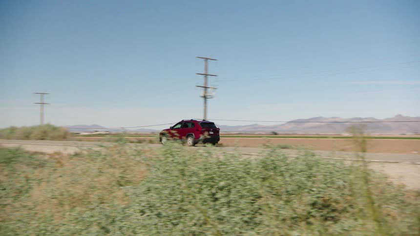 A red SUV crosses the state line into California, passing the iconic "Welcome to California" sign on a sunny day