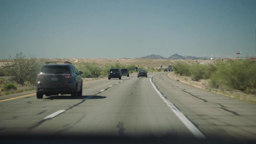 A driver's point-of-view of traveling along a sun-drenched desert highway with mountains in the distance