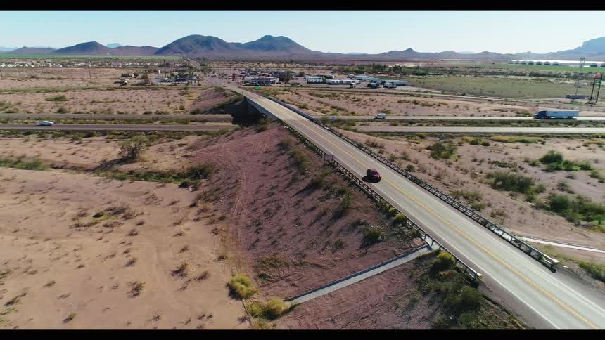 Slow aerial pull-back of a desert overpass with cars and trucks driving on the highway in a rural landscape with distant mountains