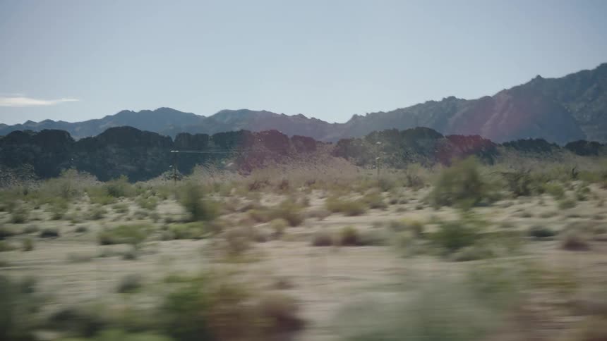A scenic drive through a sunny desert landscape with a rocky mountain range in the background