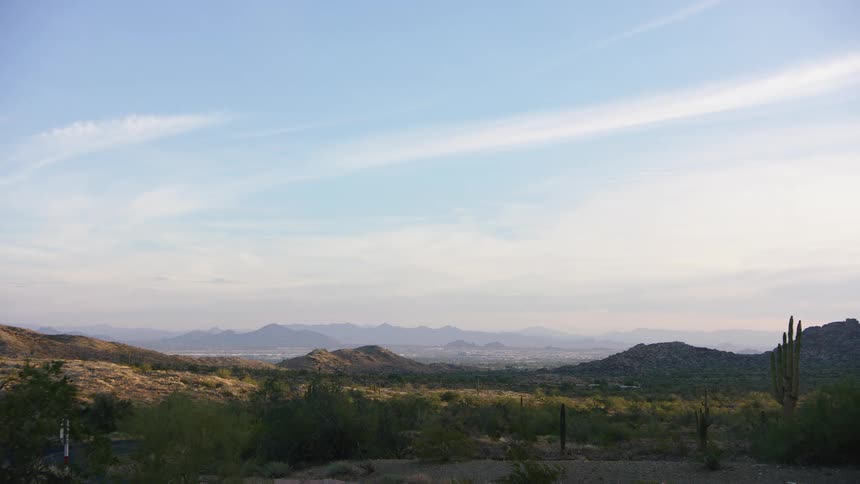 A white pickup truck drives along a dirt road through the expansive Arizona desert landscape with a city visible in the distant valley