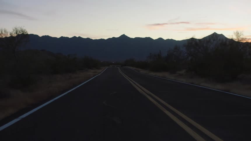 A cinematic first-person view driving down a remote desert road at twilight with mountains on the horizon