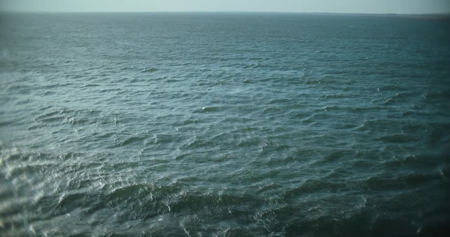 A slow pan reveals the vast, choppy surface of the deep green ocean under a hazy sky