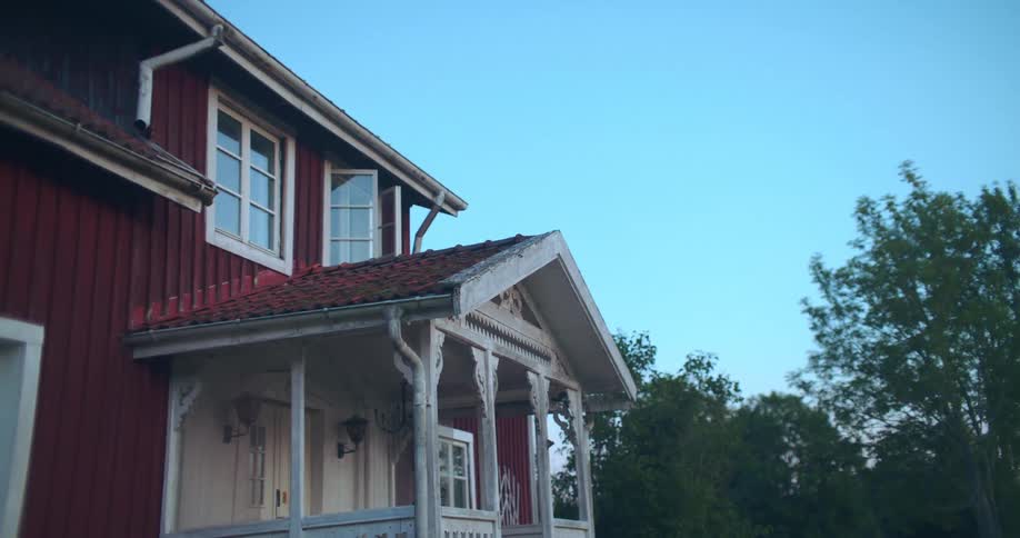 A classic red Scandinavian country house with white trim stands peacefully against a clear evening sky