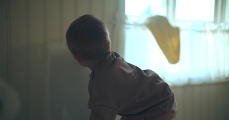 A curious toddler in a diaper carefully climbs onto the toilet seat in a naturally lit bathroom