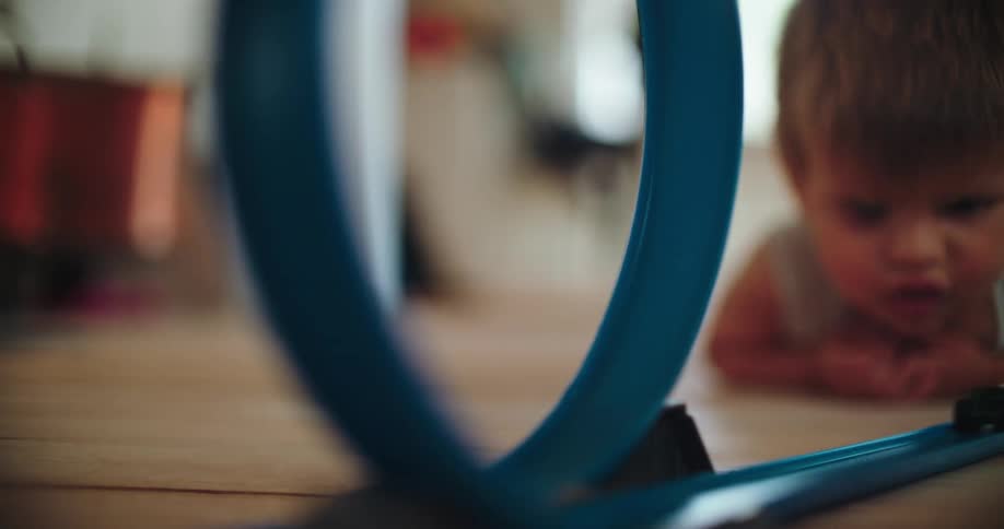 A young boy watches intently as his toy car completes a loop on a blue racetrack in slow motion