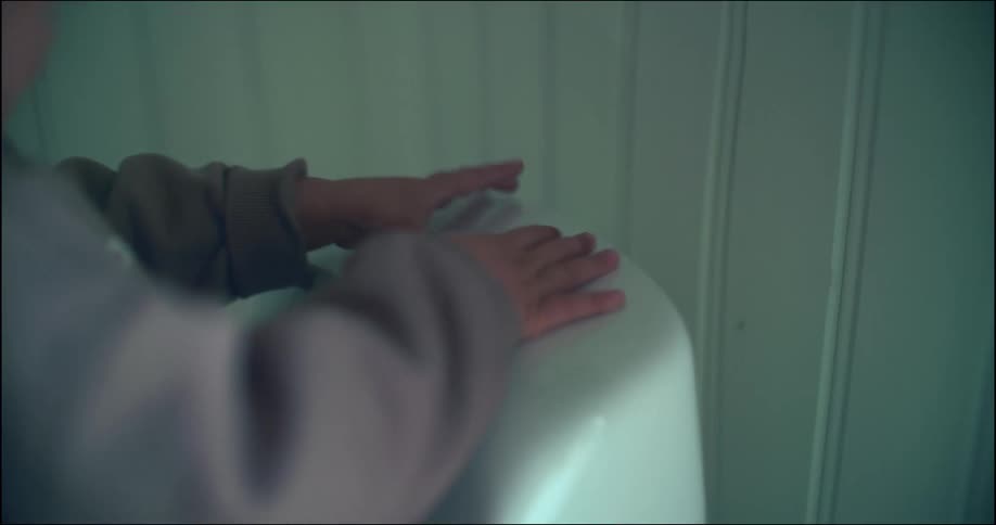A child dries their hands using a wall-mounted hand dryer in a public restroom