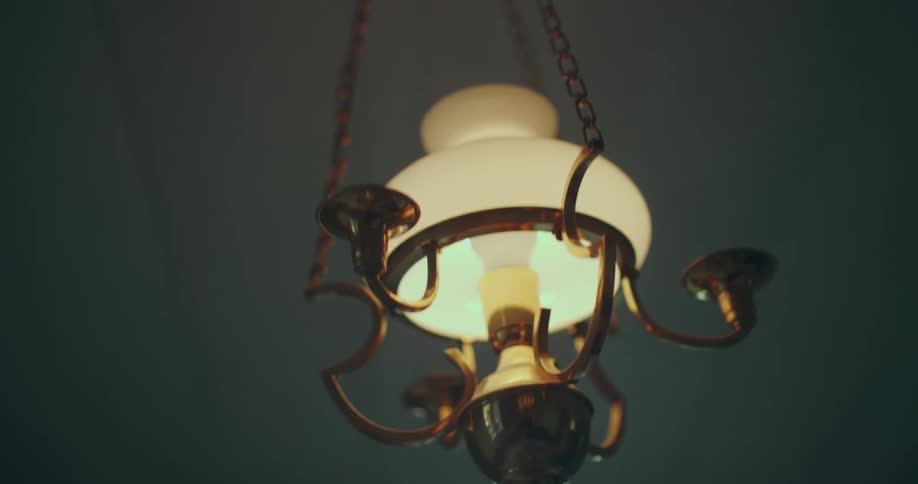 Low angle shot of a vintage hanging lamp swinging back and forth in a dimly lit room