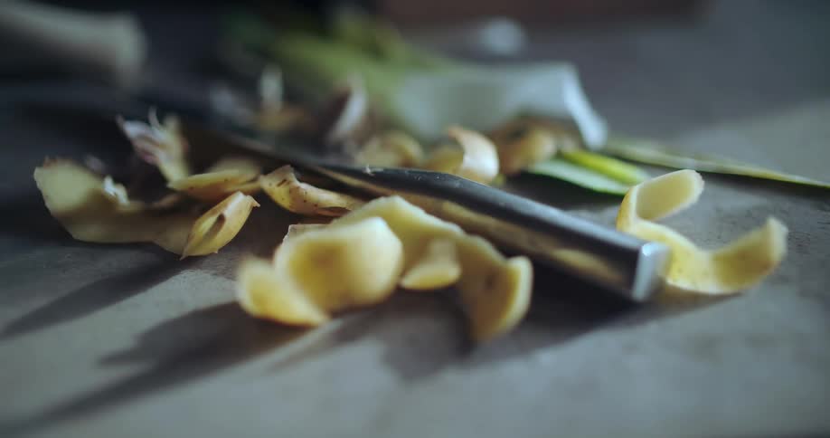 A close-up still life of potato peels and a vegetable peeler on a kitchen countertop