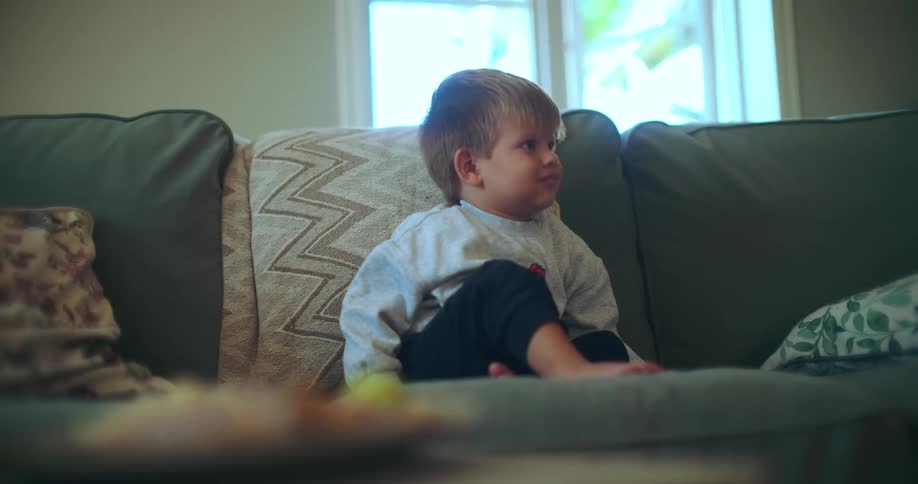 A cute toddler sits on a couch, engrossed in watching television in the living room